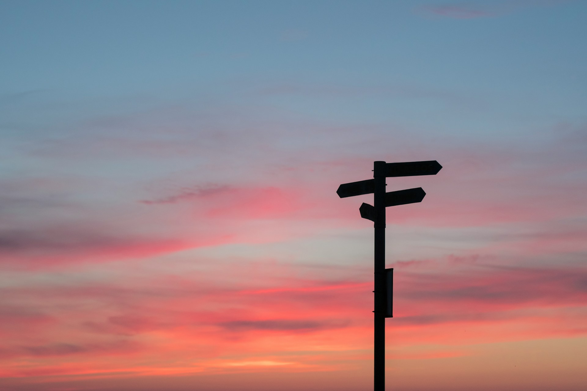 Sunset behind signpost pointing in different directions.
